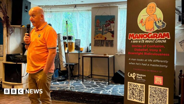 A bald man in an orange polo shirt talks into a hand held microphone