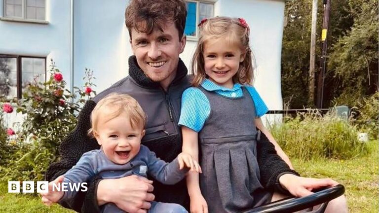 Terminally ill Devon dad says ‘I want to see my children grow’ A young dad is sitting on a red ride-on lawn mower with his two children in his lap. One is a young blonde boy aged around 16 months, the other is a five-year-old girl with light brown hair in plaits. The girl is wearing her school uniform.