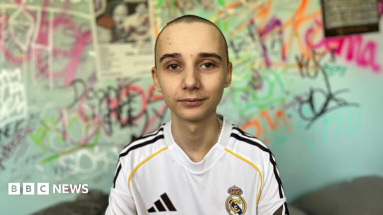 Bromsgrove cancer teen helps others find stem cell donors Leo sits on his bed in his bedroom, behind him is a colourful graffiti wall. He is wearing a signed Real Madrid top which was gifted to him by Jude Bellingham. He has a buzz cut.
