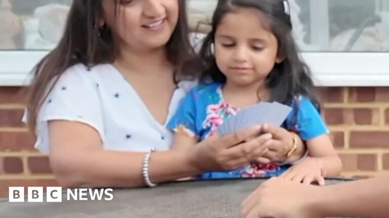 A woman sits with her daughter at a table outside.