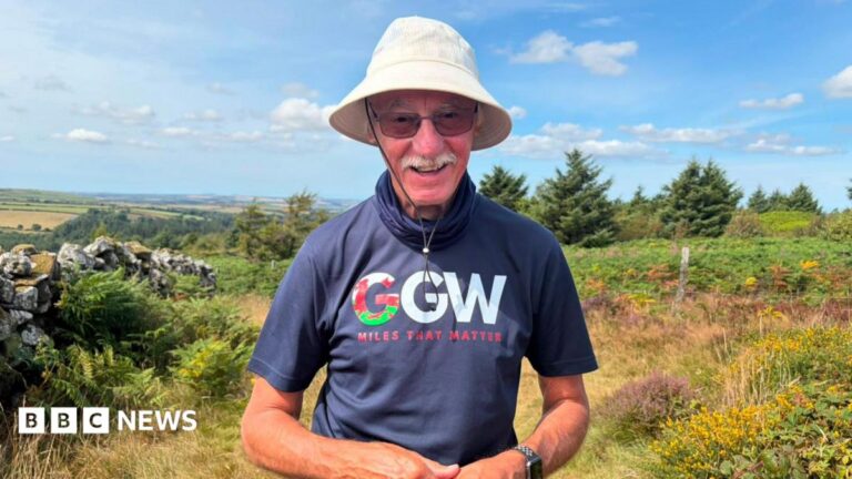 Pontypool granddad with cancer risks his health to help others John Parry stands smiling at the camera, with a view of north Pembrokeshire and the Pembrokeshire coast behind him. John is wearing a 'grandad's great walk' fundraiser logo t-shirt, with sunglasses and a sun hat. He wears sunglasses and a white moustache.