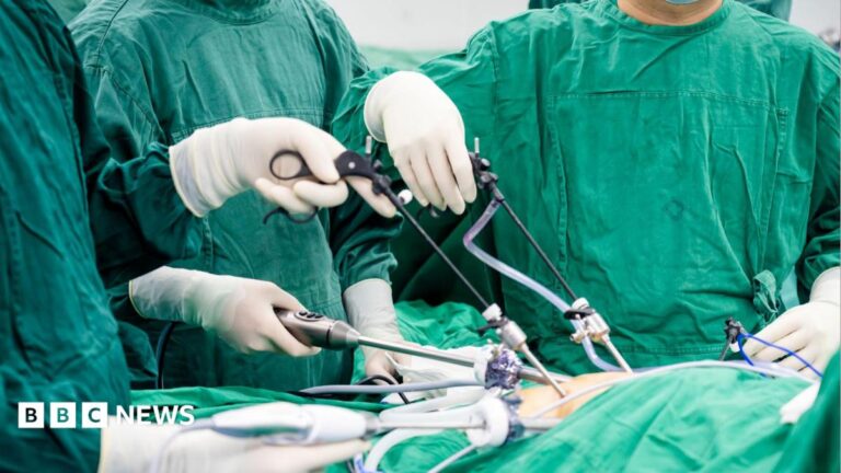 Rectal cancer trial offers non-surgical treatment hope Stock photo shows a person looking down as they hold their lower stomach while sitting on a sofa at home.