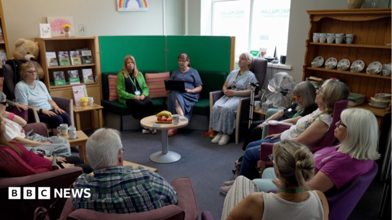 Patients sitting in a circle during one of the group sessions, with a crockery shelf to the right and a round table in the middle with a fruit bowl on it