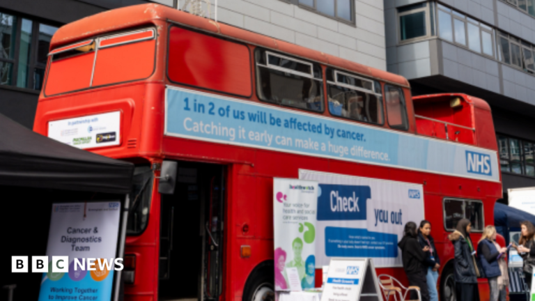 West Midlands bus tour to help people spot cancer symptoms A red double-decker bus with words on the outside including 1 in 2 of us will be affected by cancer. Some people, a chair and signs are outside the bus.