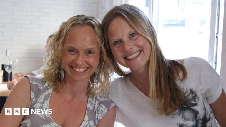 Woman changes her life after sister’s incurable cancer diagnosis Two women sit together and smile at the camera. Their heads are leaning together and they are smiling. They are in a restaurant and behind them is a table with a wine bottle and wine glass on it.