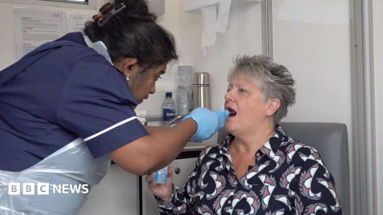 Pill on string detects oesophogel cancer in people with heartburn A woman sits in a chair with her mouth open, while a nurse in scrubs and protective clothing including gloves and an apron inserts a pill into her mouth.