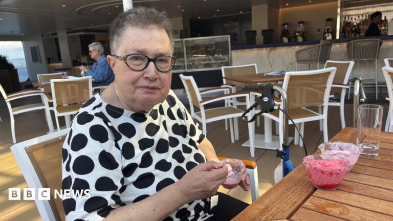 Susan Gasson smiles at an outdoor cafe table, with sunglasses pushed up on her head and a pink drink in front of her